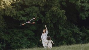 A joyful mother and child flying a colorful kite in a vibrant green park.
